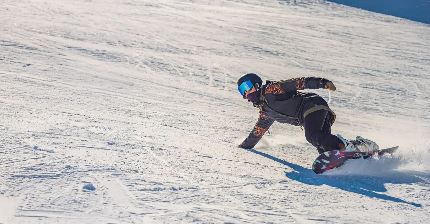 Snowboardzista w ciemnym stroju zjeżdżający po śnieżnym stoku w słoneczny dzień.