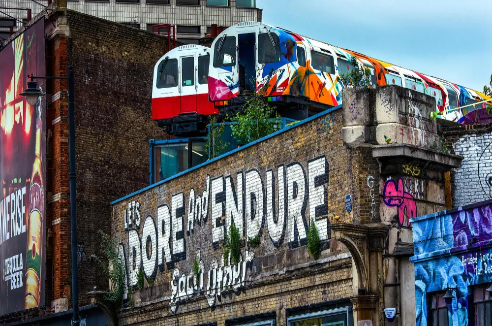 Dwa wagony metra stoją na dachu budynku, na którego ceglanej ścianie namalowano napis „Nadzieja i wytrwałość”.